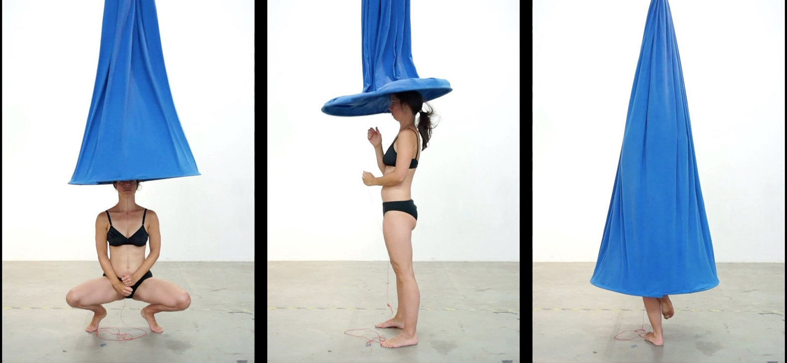 Video still from the project "Triade" by artist Maria Berauer. Three vertical video tracks lined up next to each other. Artist Maria Berauer pulling a blue fabric, which is attached to a metal ring at the bottom and hangs down from the ceiling, over her body at different heights. 
