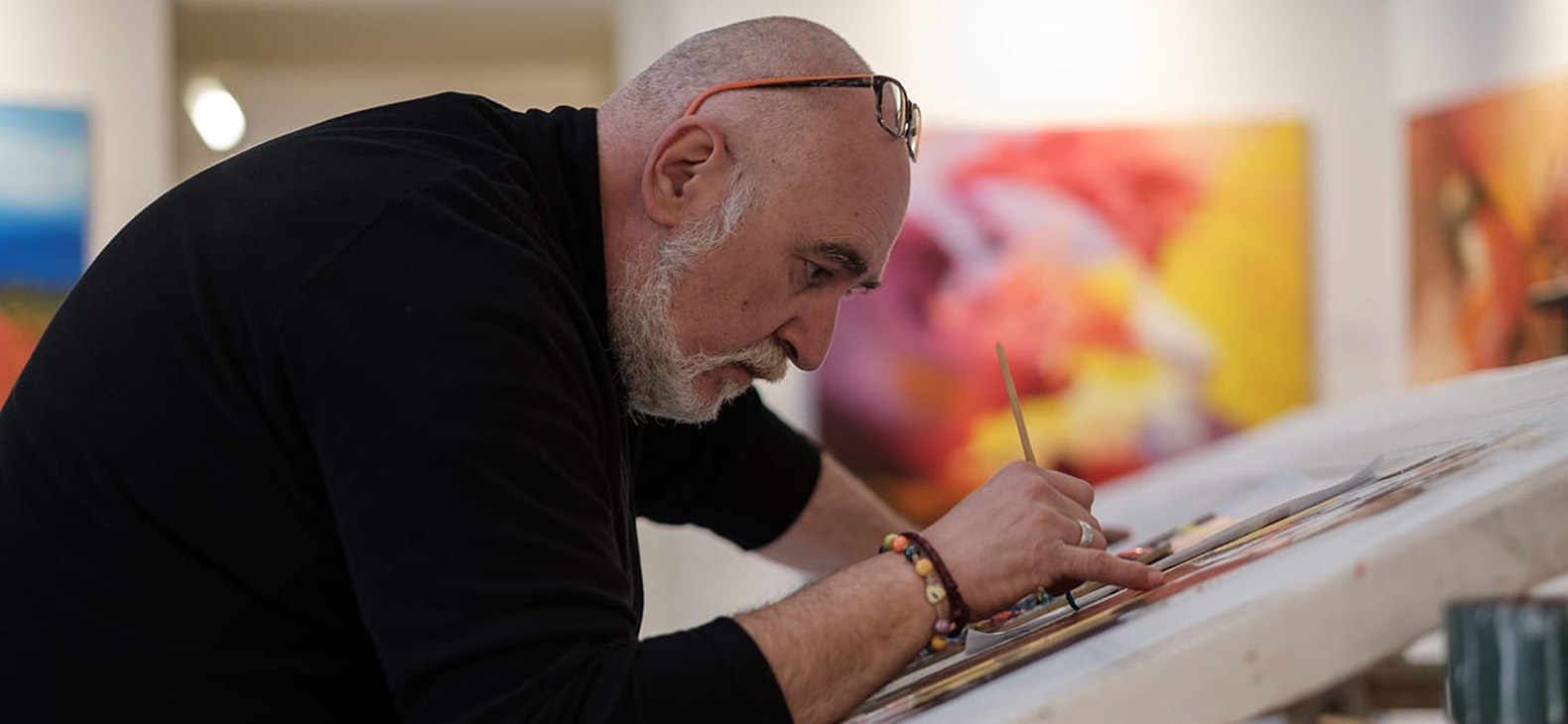 Schafhof Residency Program; Artists 2022: Michele Gomez. Italian artist Michele Gomez is seen working on one of his paintings. He can be seen in side profile leaning over the painting.