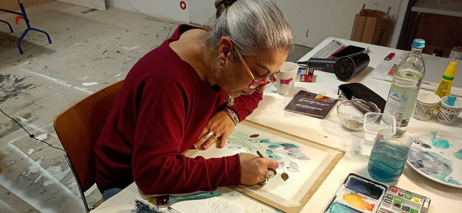 Schafhof Residency Program; Artists 2022: Carmen Toscano. Italian artist Carmen Toscano is seen working on a watercolor painting. She can be seen leaning over the painting from an angle.