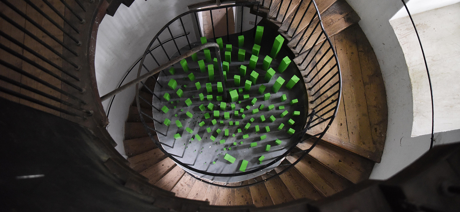 Schafhof Residency Programme; Artists 2023: Margit Greinöcker, picture: "Green City", installation made of green lacquered old wood on the floor of a round old building staircase as part of the exhibition TUERMEN, Linz 2022; bird's eye view photography in the staircase (photos: Ophelia Pauline Reuter).