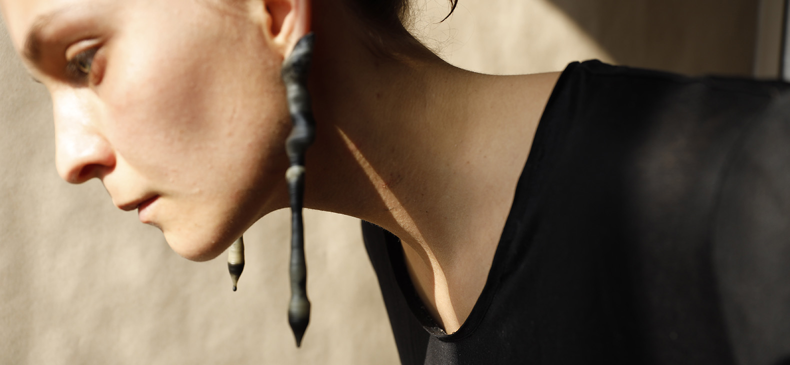 Artist-in-Residence: Camilla Prey, Focus > Limassol, residency in Limassol August - September 2023: Image: photo of a work by the artist; A woman bent forward with long, fancy, teardrop-shaped earrings can be seen from her eyebrows to her chest.