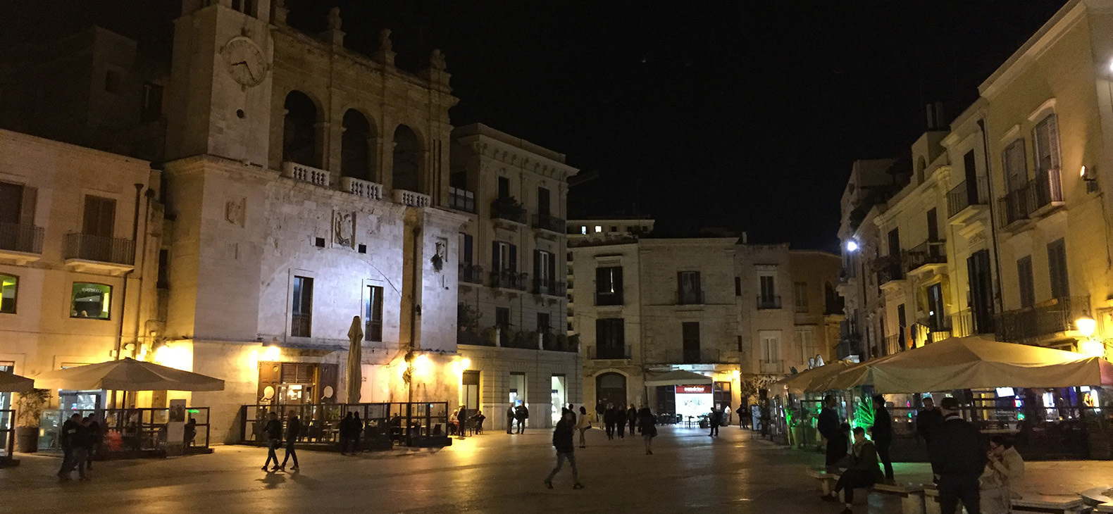Aufnahme bei Nacht von einer Innenstadt. Auf der Straße laufen Menschen